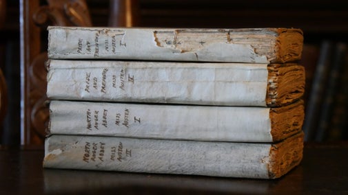 A pile of early-edition Jane Austen novels with pale white covers.